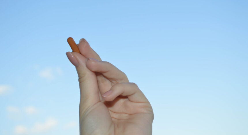 Beautiful female hand holds a medical pharmaceutical pill capsule from coronavirus covid-19 for the treatment of diseases and viruses on a blue sky background